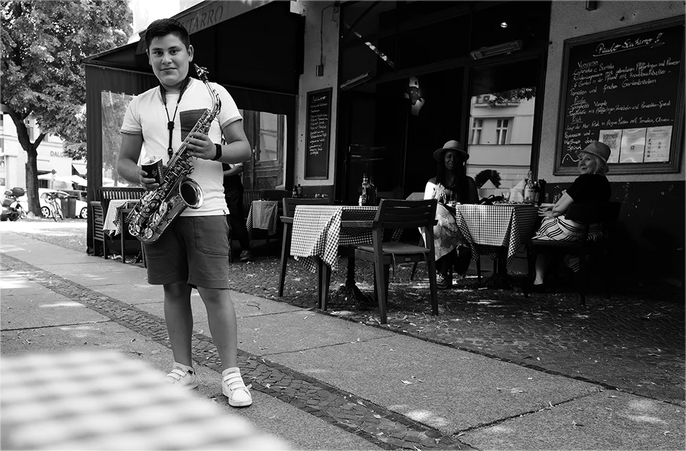Schwarzweiß-Streetfotografie mit der Leica Q3 – junger Saxophonist vor einem Café